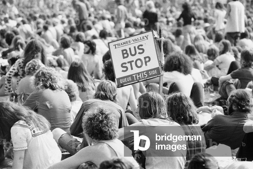 Reading Pop Festival. Festival goers with a Bus Stop sign watching the bands performing on the main stage, 24th August 1973 (b/w photo)