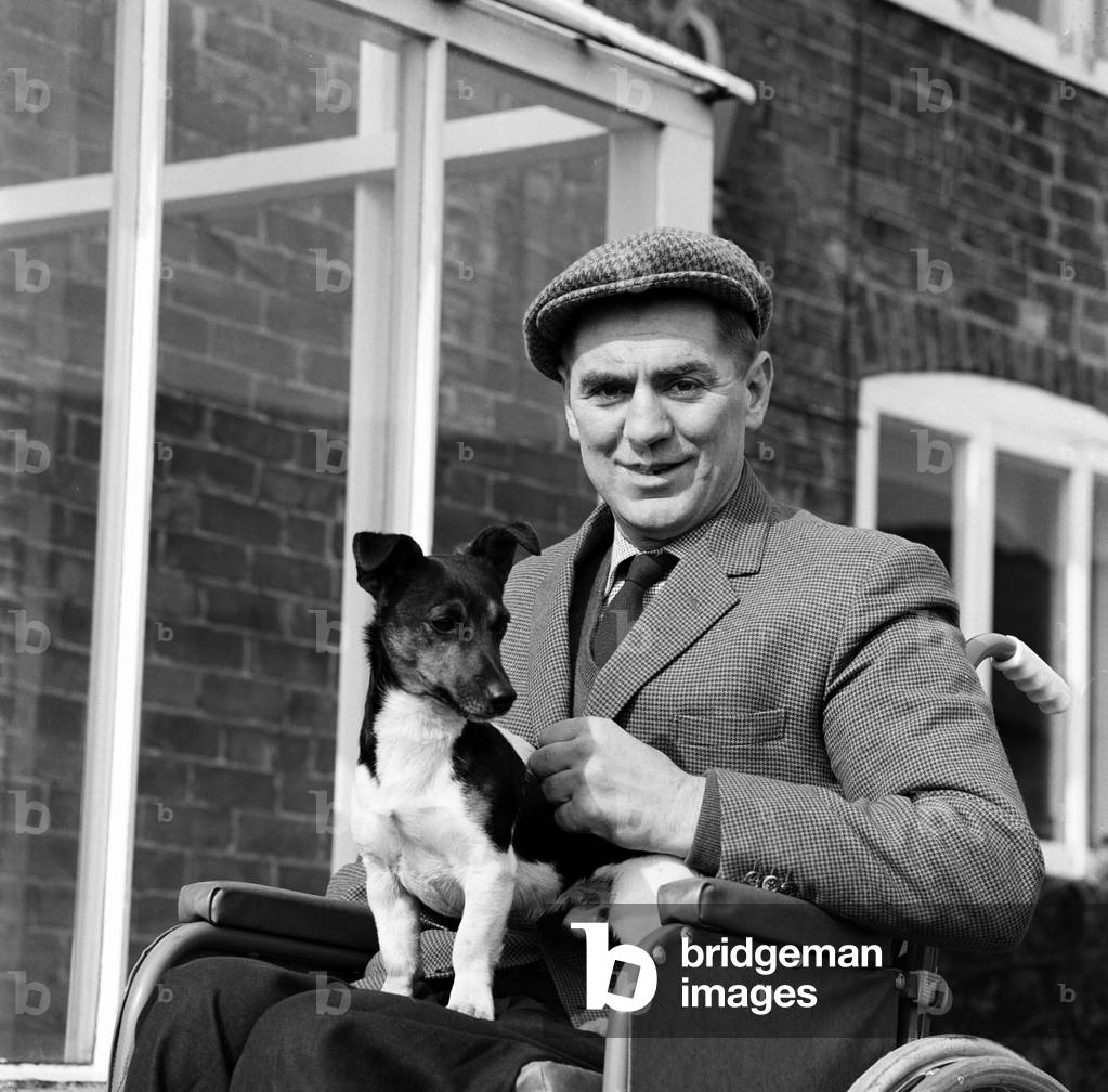 Champion Jockey Tim Brookshaw does the morning rounds at his Tern Hill, Shropshire, Farm in his wheelchair with his wife Joan. 19th March 1964 (b/w photo)