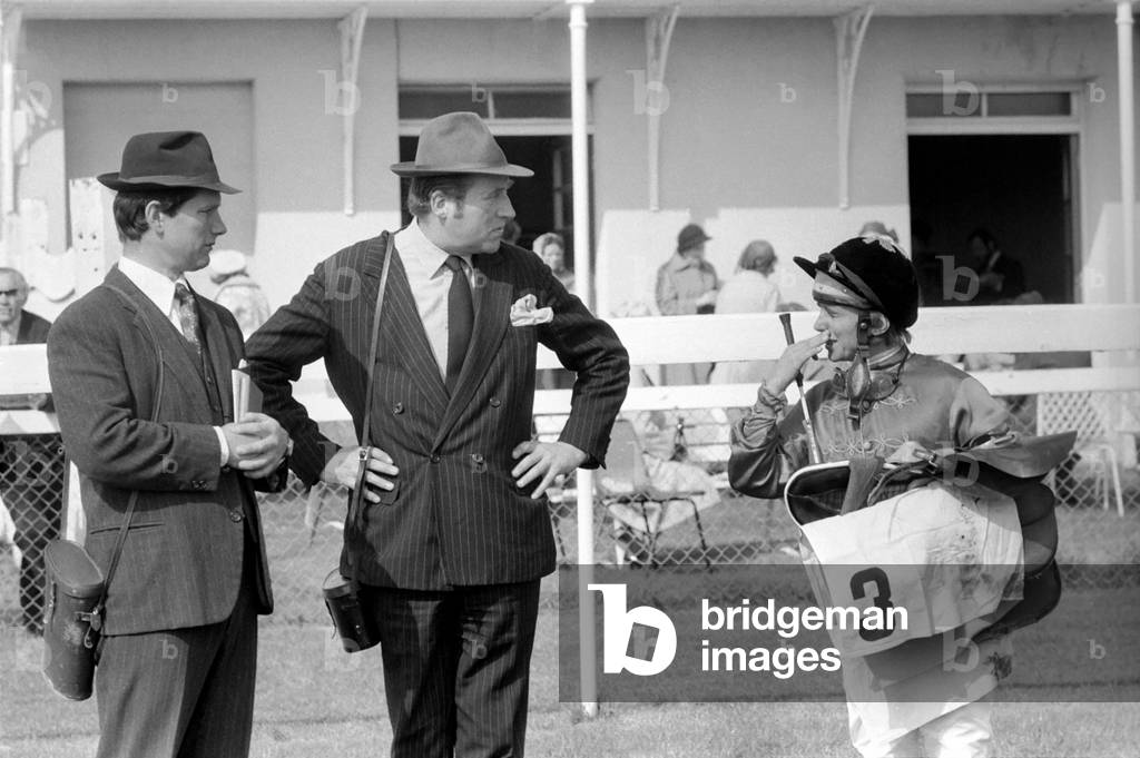 At West Ilsley, Berks trainer Major W. R. Hern stands in front of the 13 horses for the Queen, April 1977 (b/w photo)