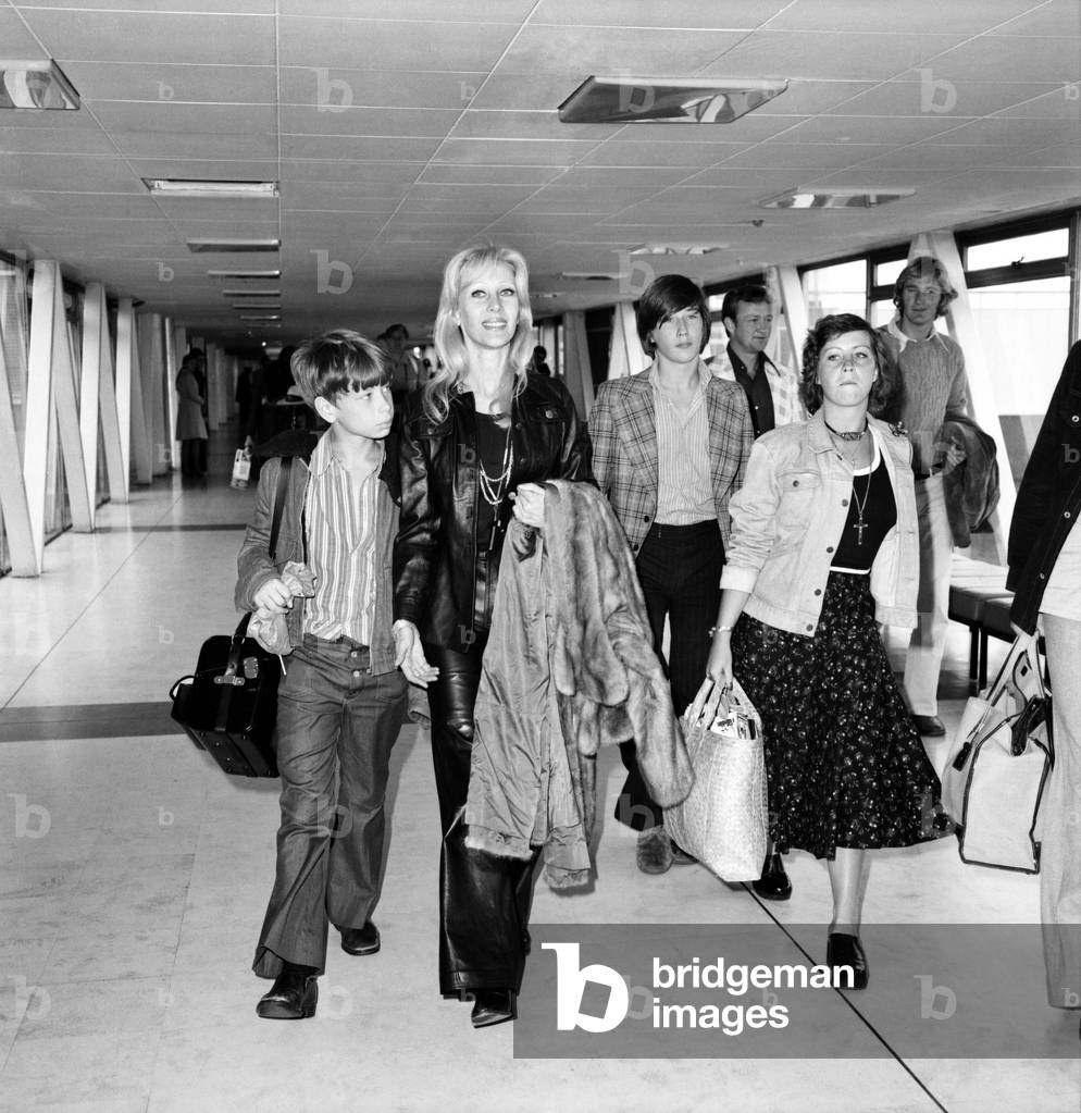 Elizabeth Harrison, wife of film actor Rex Harrison, with her three children Damian, Jared and Jamie at London's Heathrow airport, April 1975 (b/w photo)