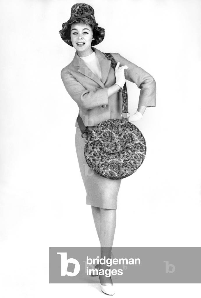 Reveille Fashions: Jackie Jackson modelling matching paisley pattern hat and handbag. October 1960 (b/w photo)