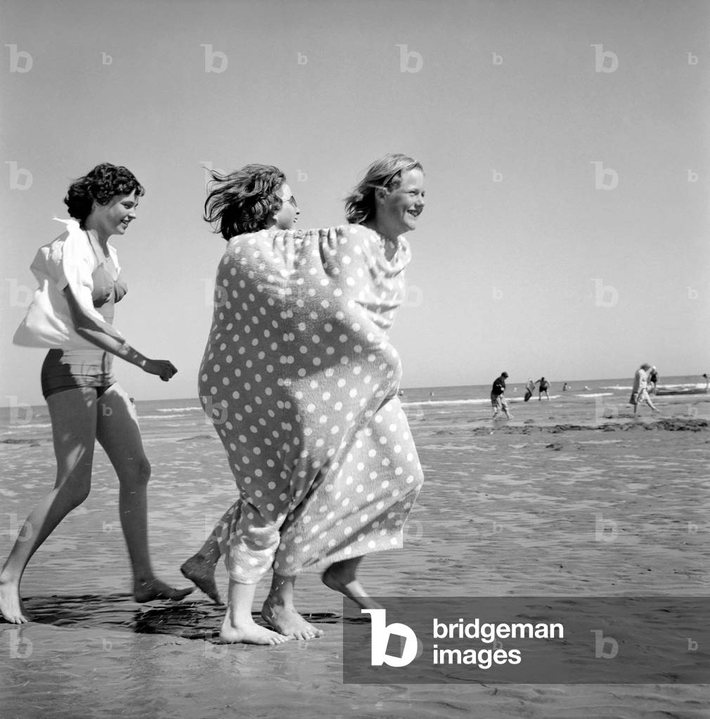 Two girls wrapped in a tent towel on the beach.