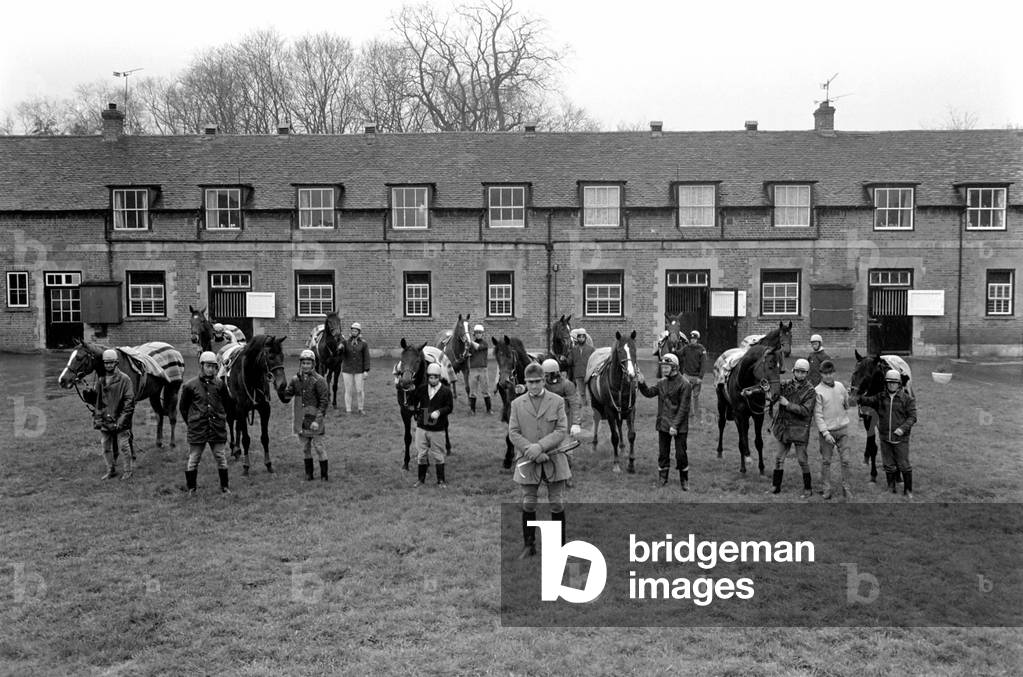 At West Ilsley, Berks trainer Major W. R. Hern stands in front of the 13 horses for the Queen, April 1977 (b/w photo)