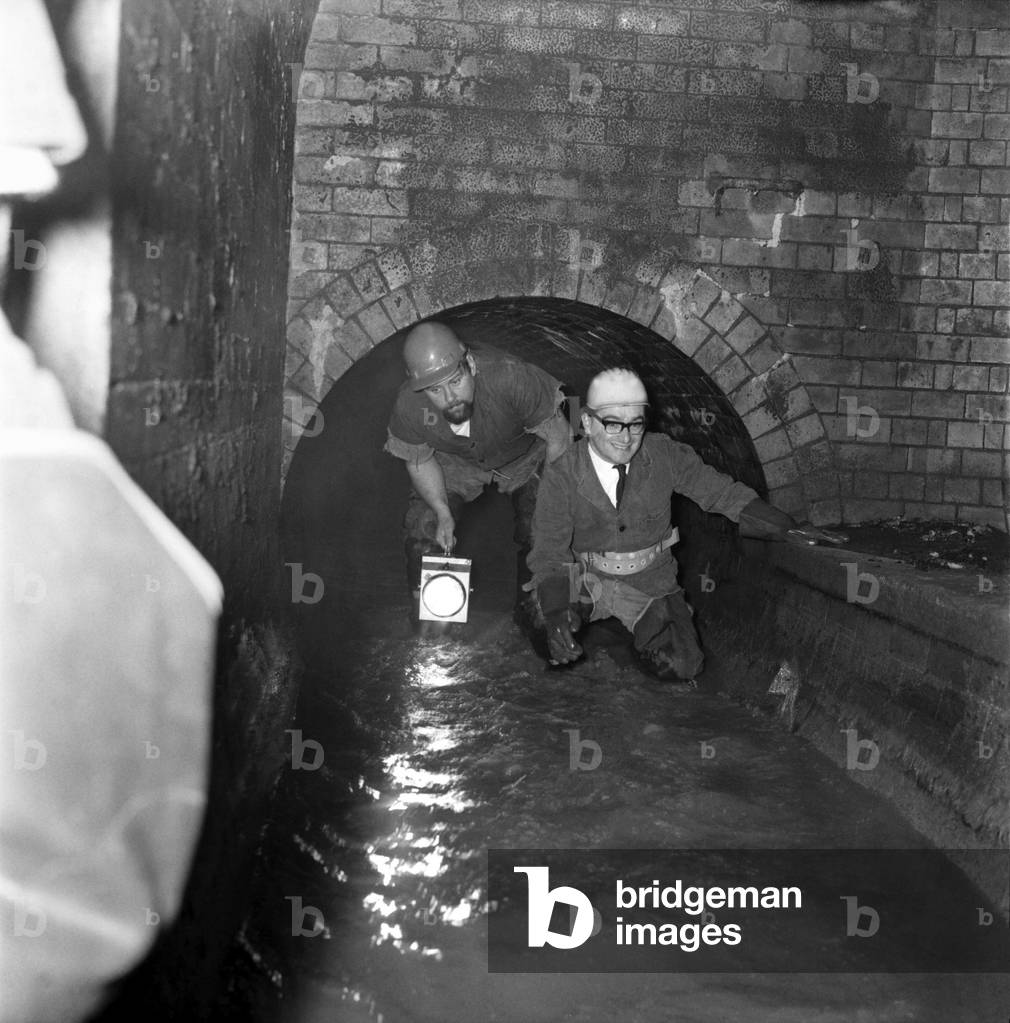 The man who wants to put the hundreds of miles of London's sewers on the map as an attraction to Londoners went below at Clampham North station and took a tour of inspection. He was Mr. Ellis Hillmann. Michael Colwell on left age 29 of Mitcham one of the sewagemen making an inspection of the brickwork. Waterfall below London. December 1969
