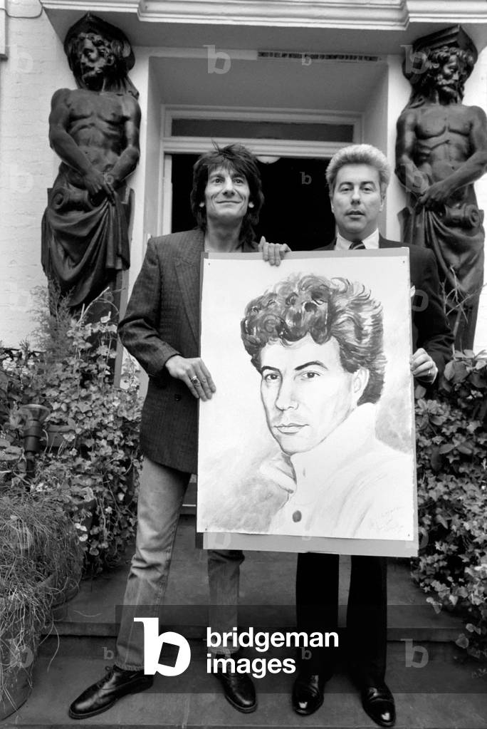 Rolling Stones: Ronnie Wood holds a painting of author Ken Follett who stands next to him. September 1987