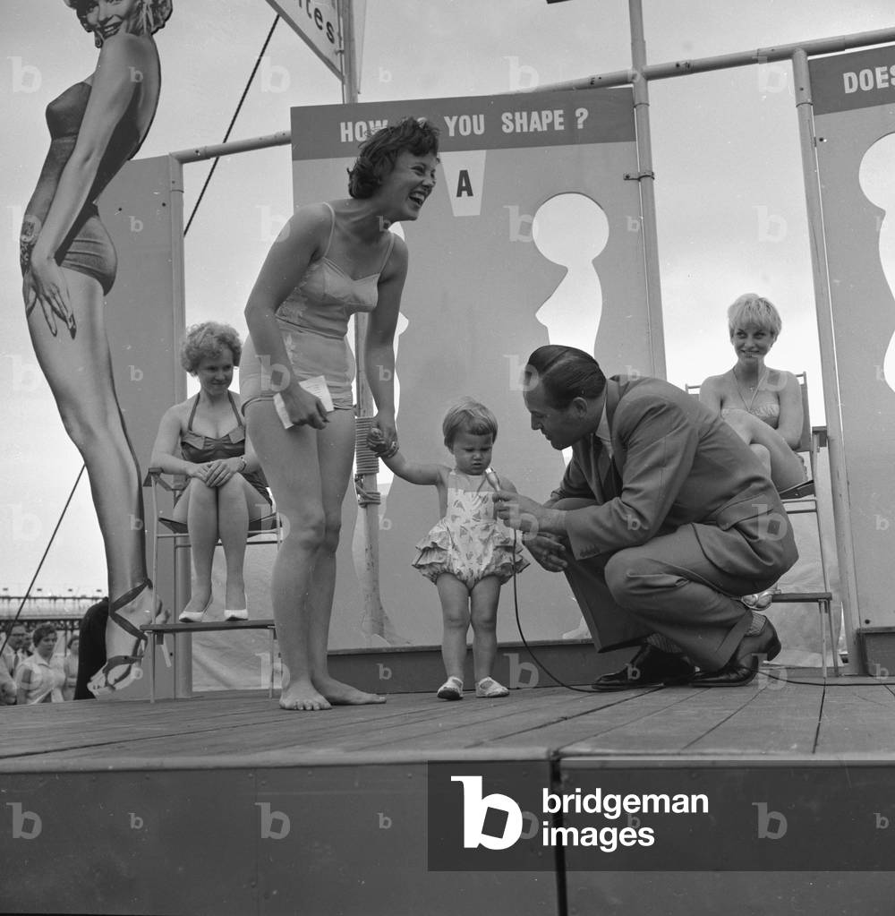 Sunday pictorial beach contest at Weston Super Mare. Mrs Anne Hewett with her 17 month old daughter on the podium where she was looked after by compere Johnny Ladd, July 1961 (b/w photo)