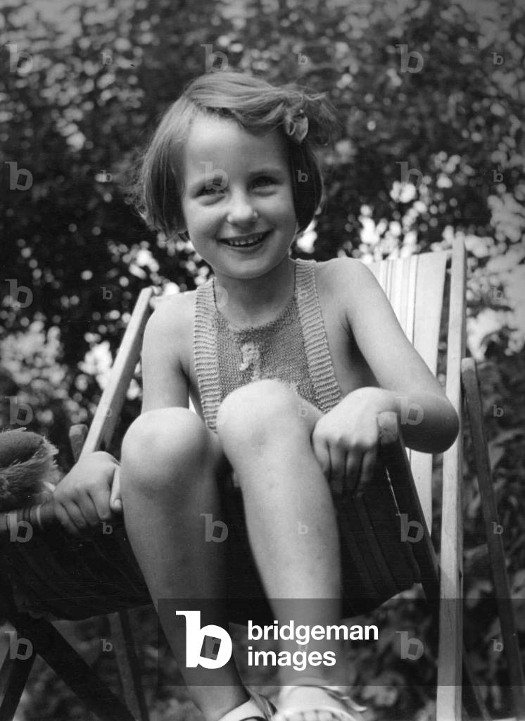 Young girl sitting in a deck chair in the back garden 
Circa 1945