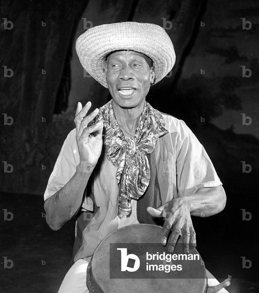 African Drummer Moses playing his instrument, November 1951 (b/w photo)