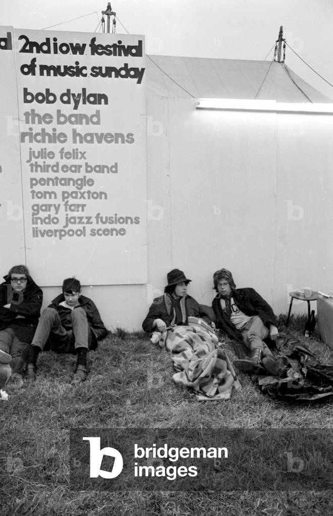 Music fans at The Isle of Wight Festival with a poster of Artists performing behind, 30th August 1969 (b/w photo)