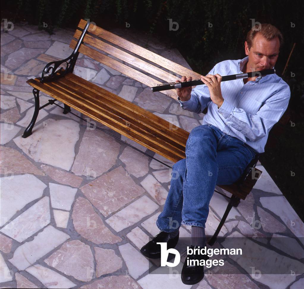 Patrick Gallois - French soloist and conductor playing the flute sitting on a bench at his home, 1994.