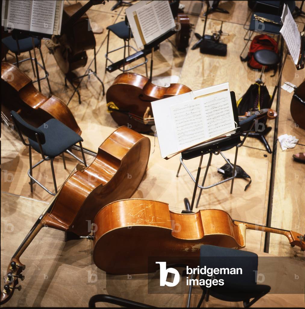 Double Basses - room with double basses resting on the floor, with music stands and musical scores.