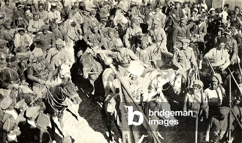 Assyrian troops led by Agha Petros (saluting) with a captured Turkish banner in the foreground, 1918 (b/w photo)