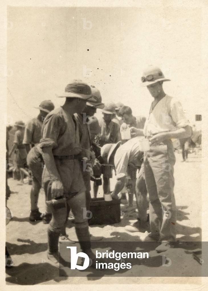 British soldiers filling their cups from a water tank in the desert, c.1916 (b/w photo)