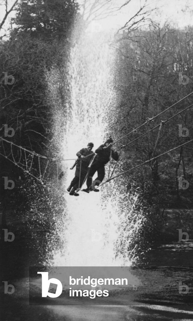 Commandos crossing a river by a Toggle bridge under 'enemy' fire, Commando Basic Training Centre, Achnacarry, Inverness-shire, c.1943 (b/w photo)