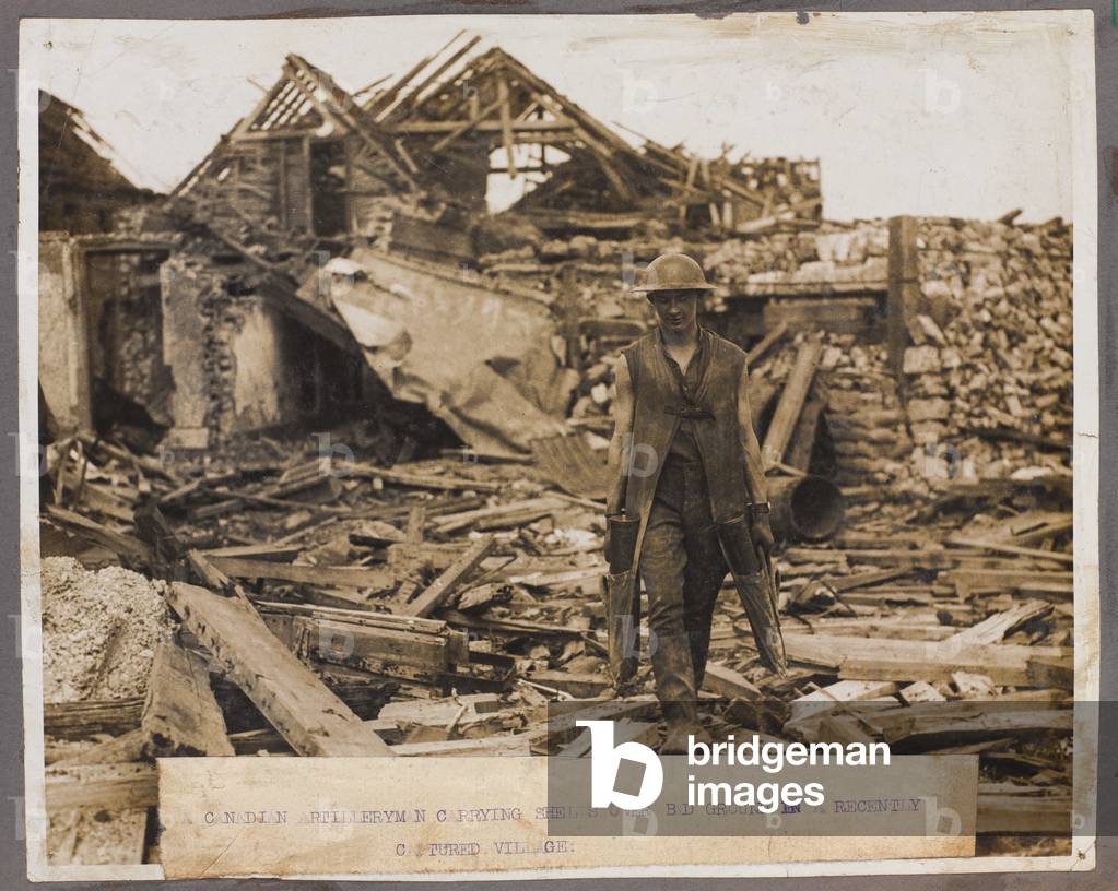 A Canadian artilleryman carrying shells over bad ground in a recently captured village, 1918 (b/w photo)