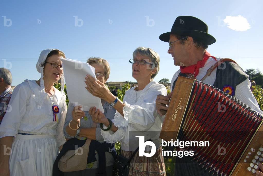 Three middle-aged women singing from song sheets accompanied by an accordionist