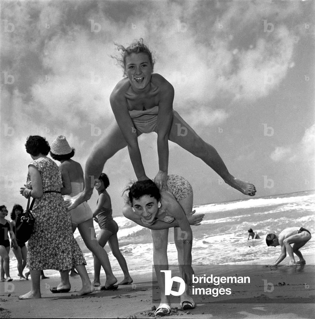 Société italienne: Viareggio, (prés de Lucques) 1956. Les jeux sur la plage : deux filles en maillot de bain jouent a saute mouton (saute-mouton) © Farabola/ Leemage