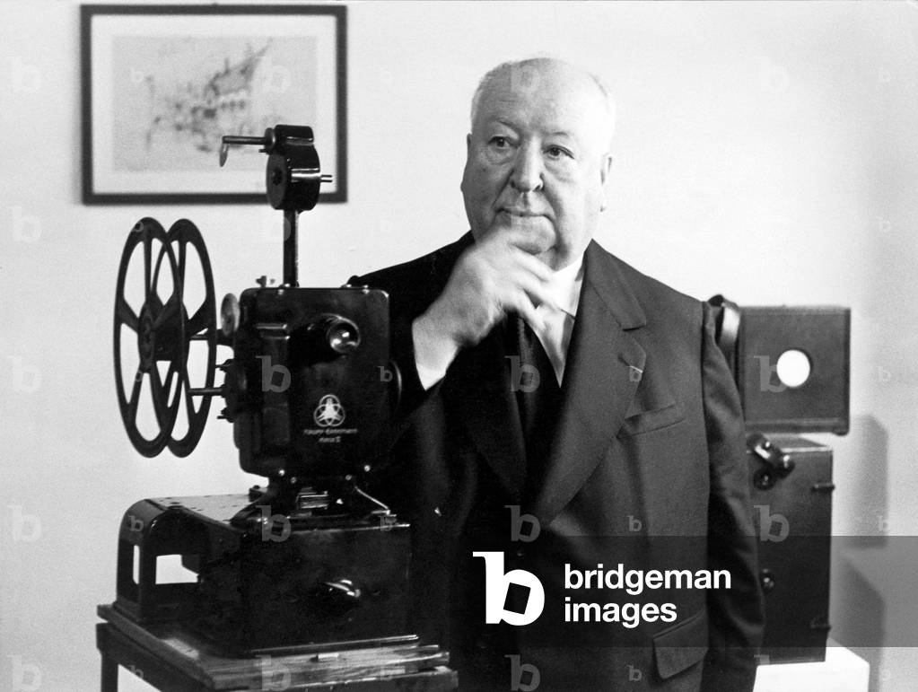Alfred Hitchcock at the cinematheque, near him a cinema projector, Milan, 1972 (b/w photo)