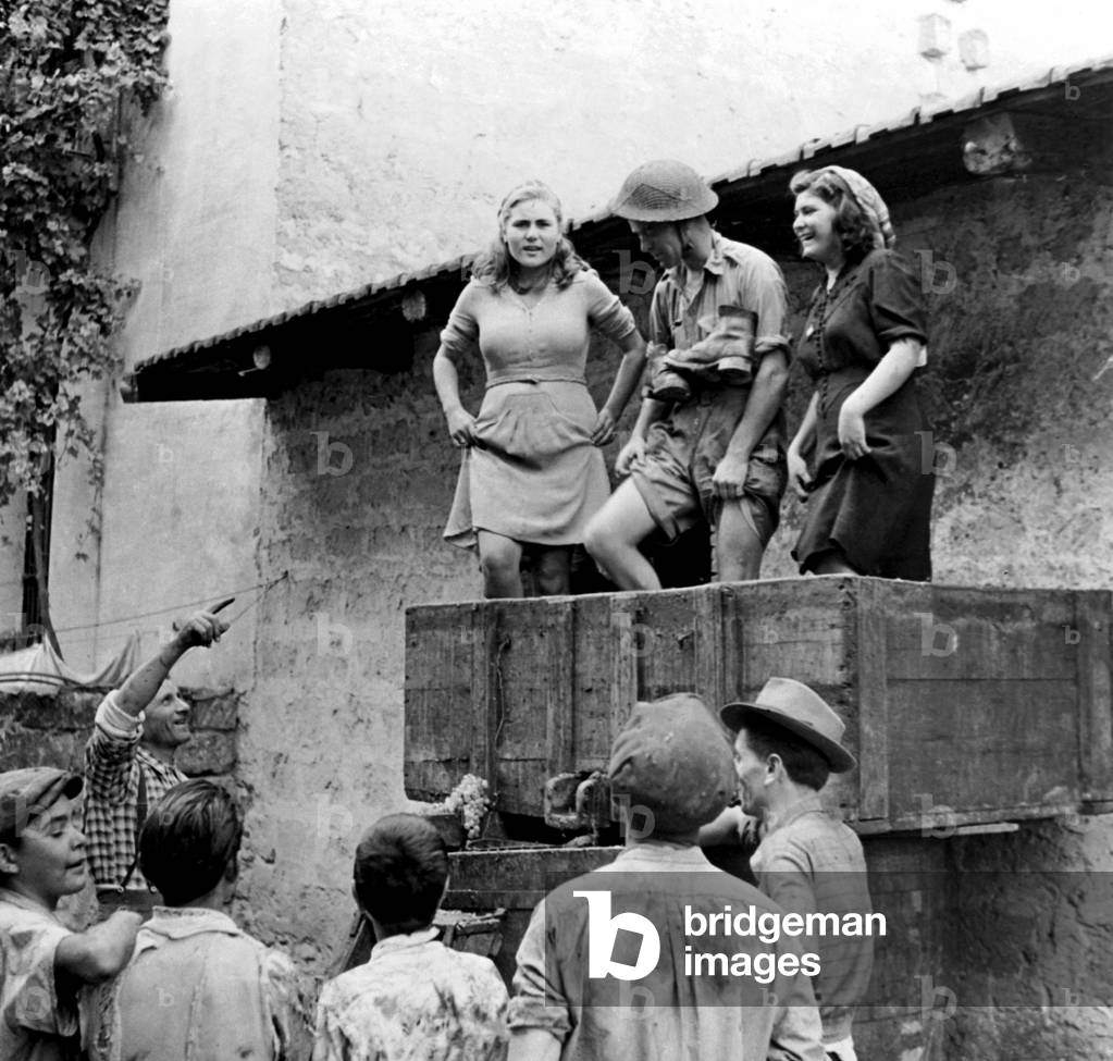 A British soldier helps women in southern Italy to crush the grapes during the harvest, 1944 (b/w photo)