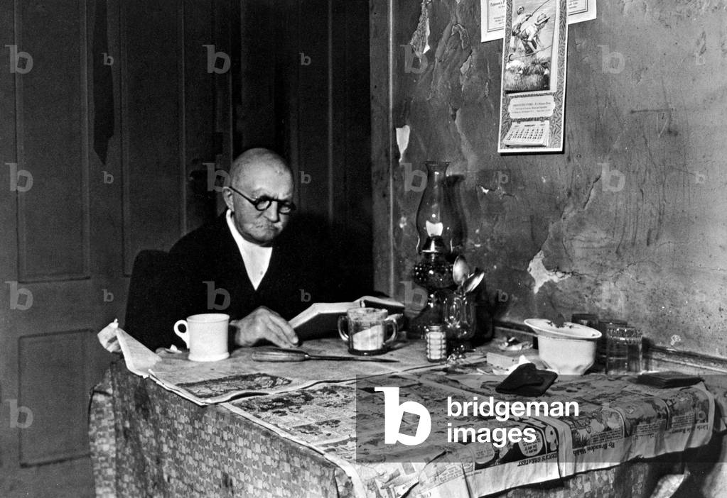 Old man reading his newspaper in his kitchen, USA, 1936 (b/w photo)