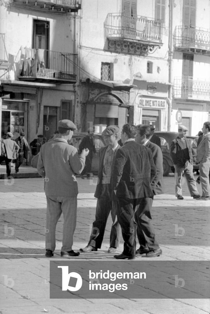 A group of men talking in a square, Sicily, 1960s (b/w photo)