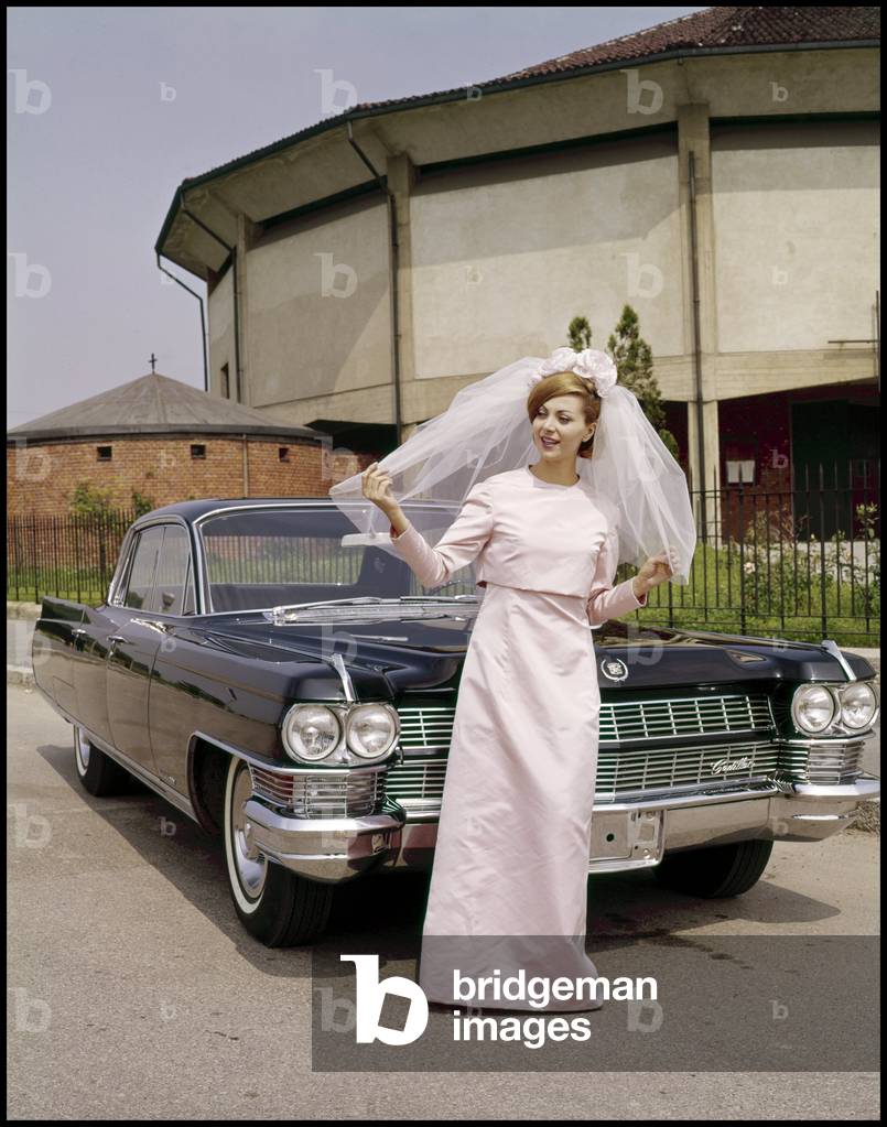 Model in wedding dress posing next to a Cadillac Fleetwood, 1964 (photo)