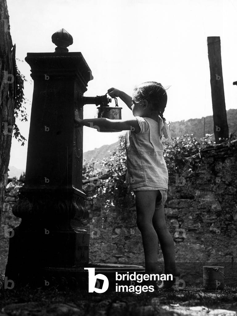 A little girl taking water at the fountain, Milan, 1947 (b/w photo)
