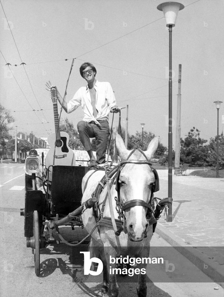 Peter Fonda riding in a horse-drawn carriage with his guitar, Venice, 1966 (b/w photo)