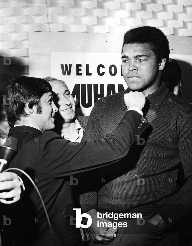 Muhammad Ali and journalists gently jostling him during an interview (b/w photo)