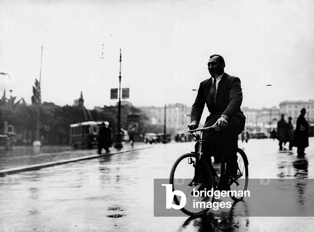 Primo Carnera riding a bicycle on piazza dei Cinquecento, Rome, 1939 (b/w photo)