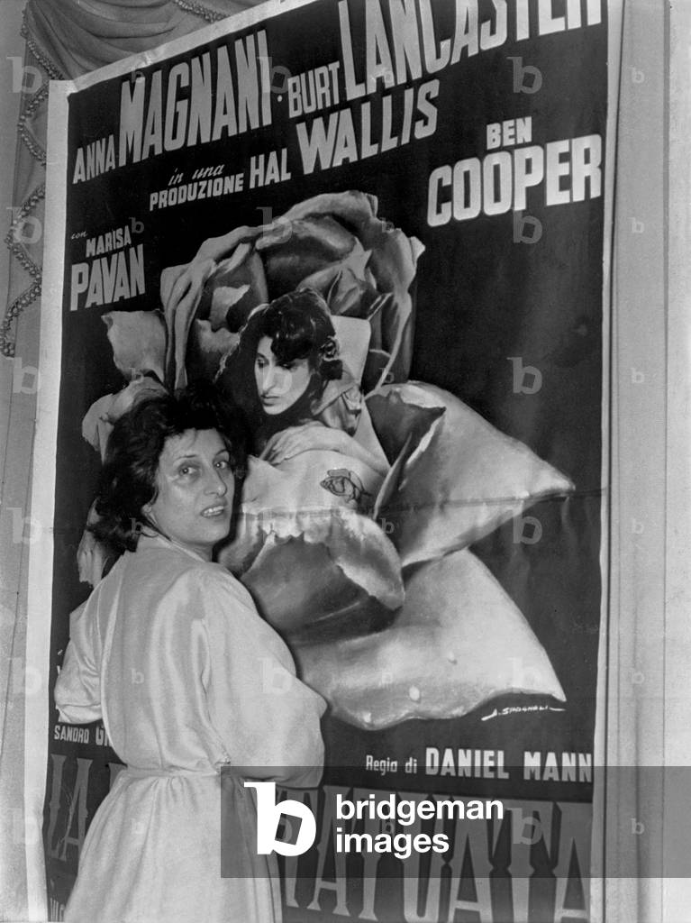 Anna Magnani posing at home in front of the poster for the film 'La Rosa Tatuata', Rome, 1956 (b/w photo)