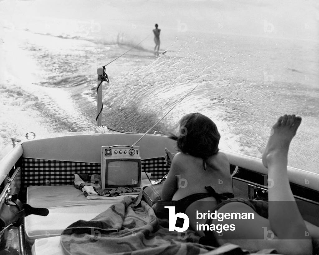 Young woman in bikini watching a portable TV on a boat, 1965 (b/w photo)