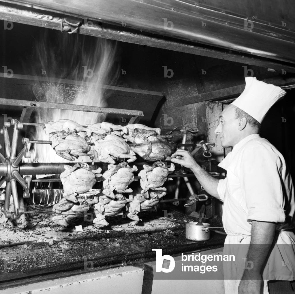 The cook of a rotisserie controlling the cooking of chickens, roasted on a spit, 1951 (b/w photo)