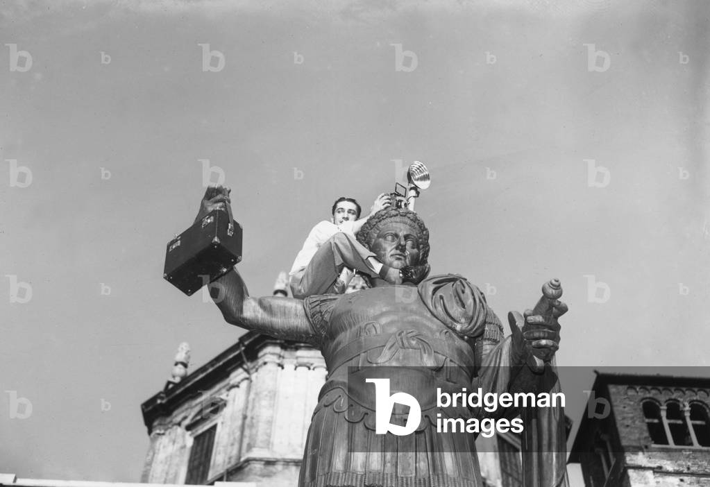 Tullio Farabola perched on the statue of Constantine in San Lorenzo Square, Milan, 1949 (b/w photo)