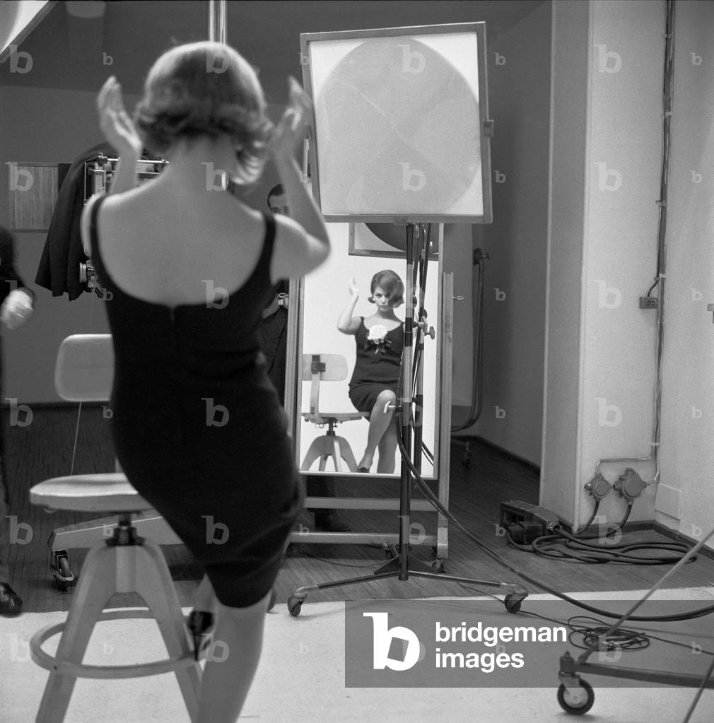 Claudia Cardinale fixing her hair in a mirror before a photo shoot, Milan, Italy, 1964 (b/w photo)