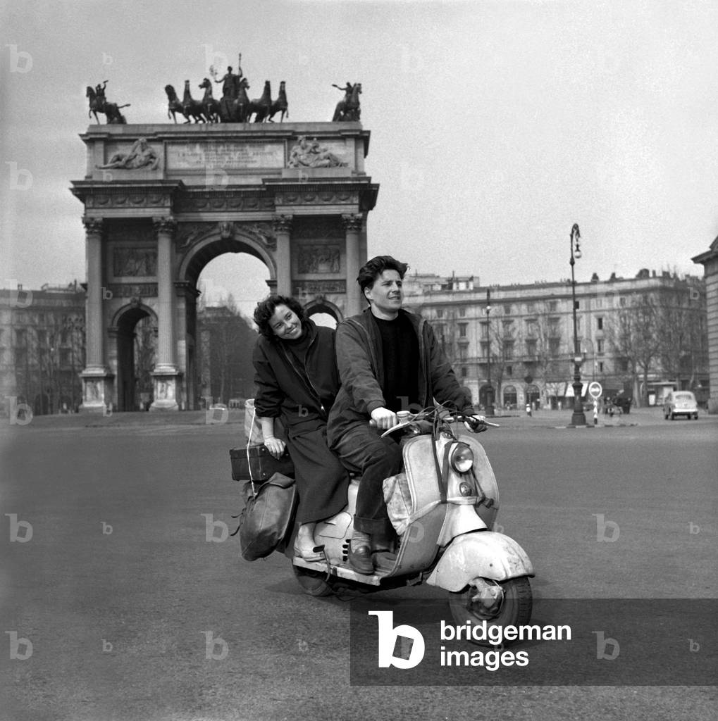 Italian couple on a Lambretta scooter in front of the Arco della Pace, Milan, 1955 (b/w photo)
