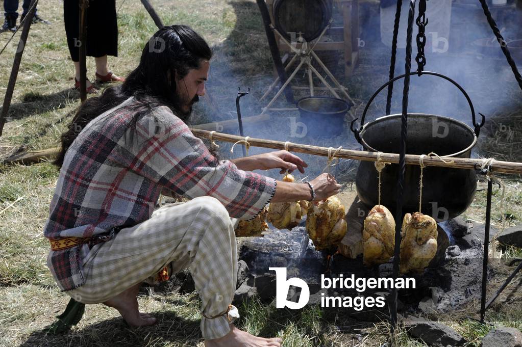 Arverniales 2017 on the site presume of Gergovia oppidum. Historical and culinary reconstitution: a participant dresses in Gallic fashion bakes chickens on the ember - cooking on wood fire, Gauls, Gaul - Auvergne, Puy-de-Dome - Photo Patrice Cartier -