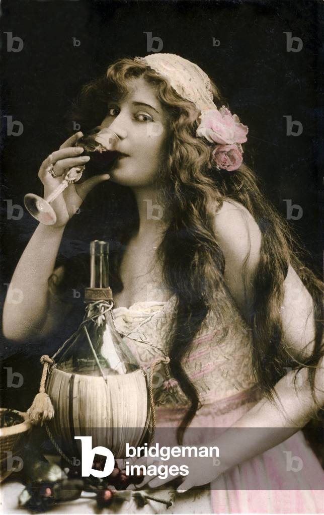 young woman has long hair drinking a glass of wine looking eager. postcard late 19th or early 20th century after a photograph of Reutlinger -