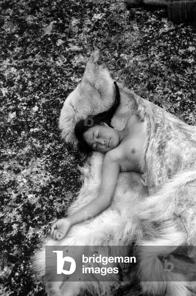 Young inuit taking a nap on a fur, during polar expedition in Greenland, Kangerdlugssuatsiak, Autumn, 1936 (b/w photo)