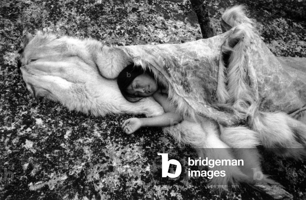 Young inuit taking a nap on a fur, during polar expedition in Greenland, Kangerdlugssuatsiak, Autumn, 1936 (b/w photo)