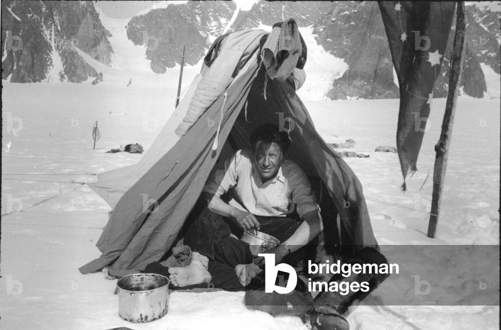 Paul-Emile Victor at the bivouac. Near him, the flag he had made for TransGreenland (July 1936), Mount Forel, Greenland, June 1937 (b/w photo)