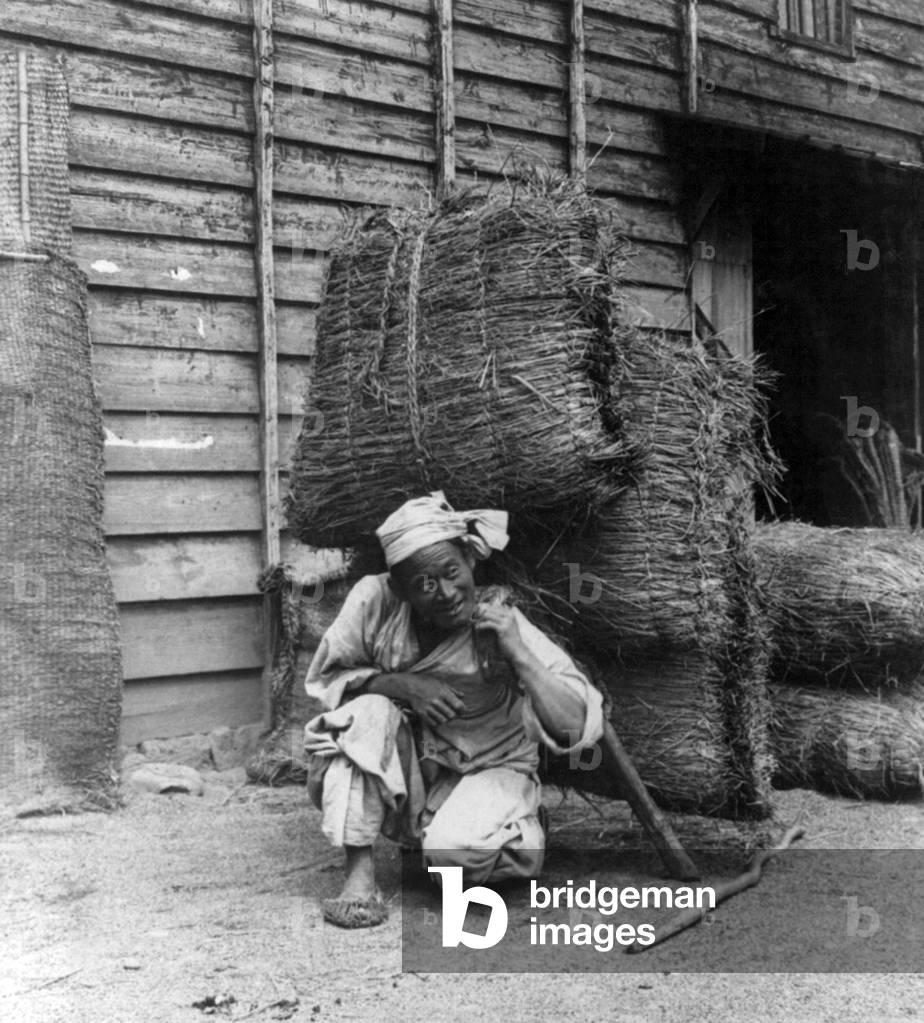Korea: A coolie re-adjusting his pack, Seoul, early 20th century