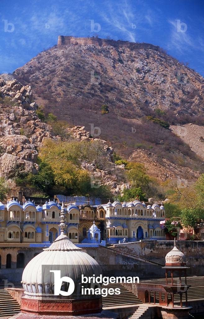 India: The walled fortifications of the Bala Qila (Alwar Fort) loom above the huge kund (tank) next to the Vinay Vilas (City Palace), Alwar, Rajasthan
