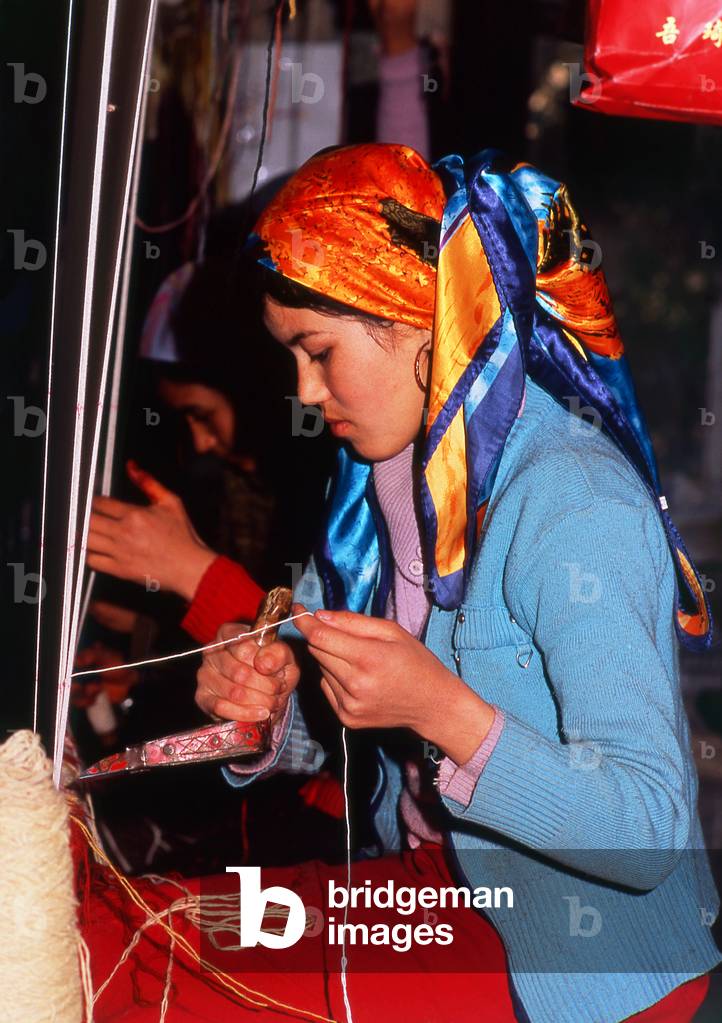 China: A Uighur carpet weaver, carpet factory, Khotan, Xinjiang