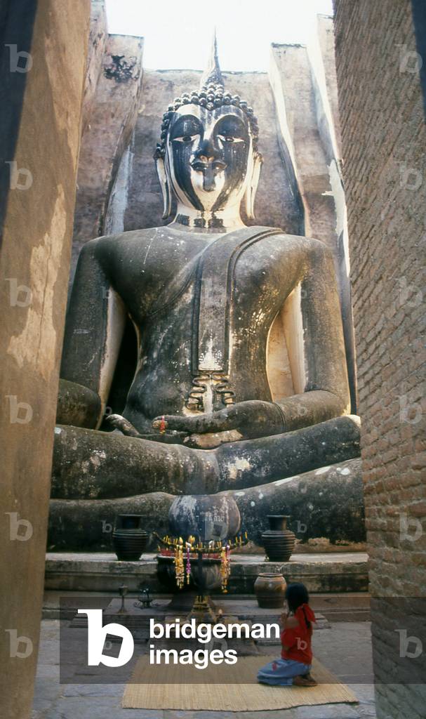 Thailand: A young girl pays her respects to the 15 metre high seated Buddha, Wat Si Chum, Sukhothai Historical Park