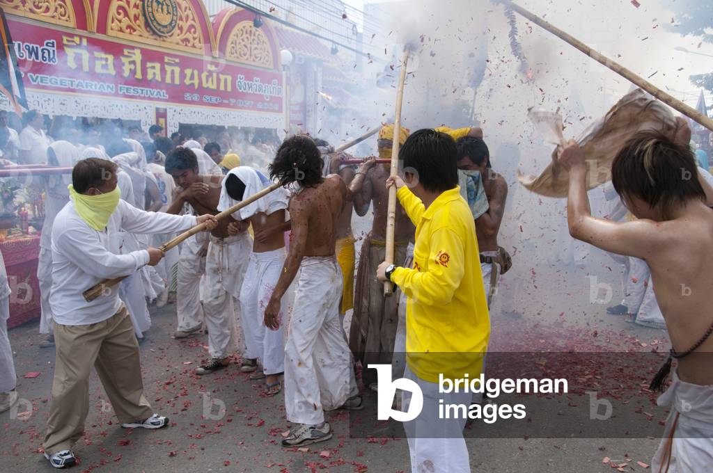 Thailand: Shop owners wave bamboo poles with strings of exploding firecrackers over the heads of shrine bearers, Phuket Vegetarian Festival