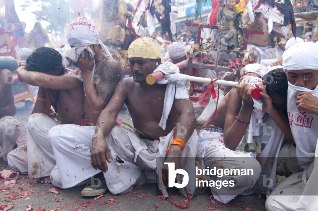 Thailand: Shop owners wave bamboo poles with strings of exploding firecrackers over the heads of shrine bearers, Phuket Vegetarian Festival