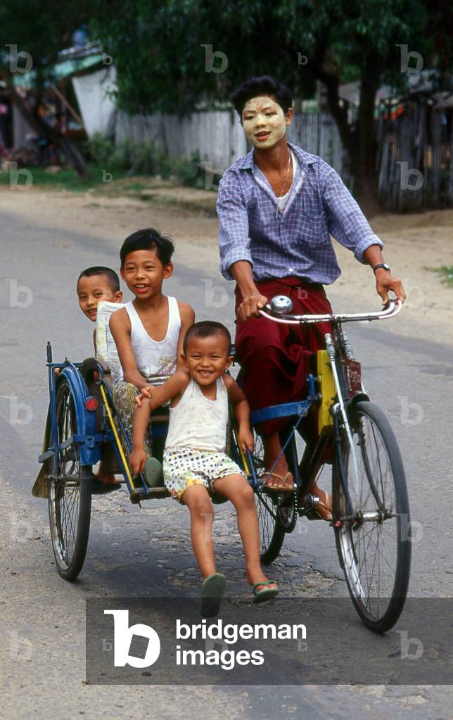 Burma / Myanmar: Three Bamar children riding a bicycle rickshaw, the driver's face protected by thanaka powder
