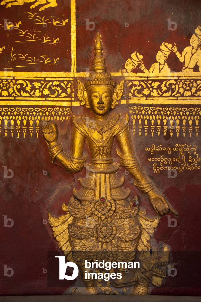 Burma / Myanmar: An 'Arhat' or 'perfected person' stands in alignment with gold stencilled ('lai kham') paintings on a wall in the main viharn at Wat In, Kyaing Tong (Kengtung), Shan State
