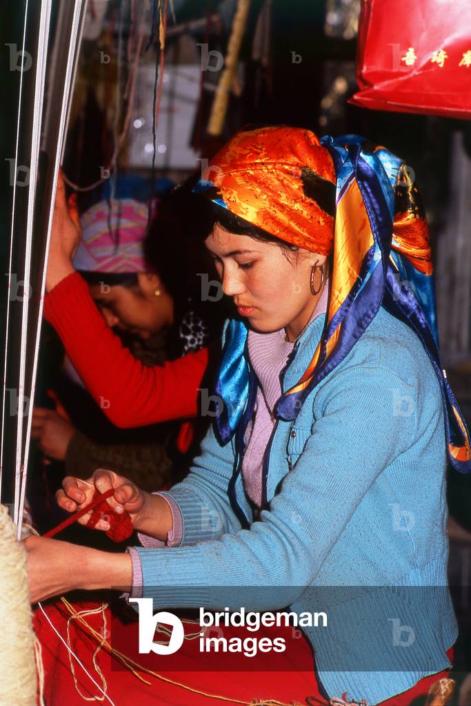 China: A Uighur carpet weaver, carpet factory, Khotan, Xinjiang